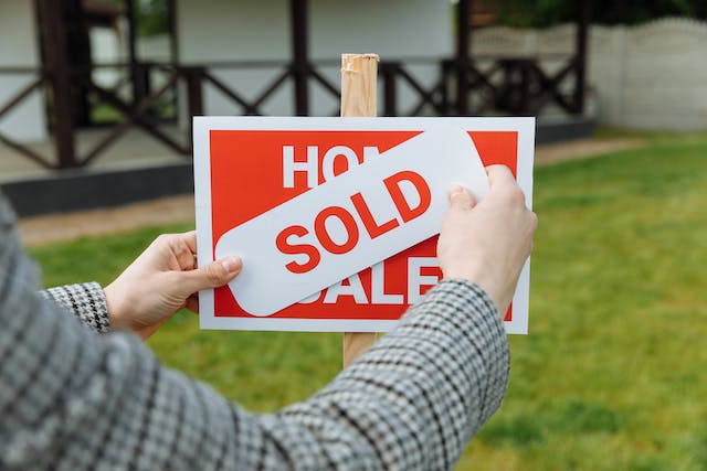 person placing a sold sticker on a home’s for sale sign